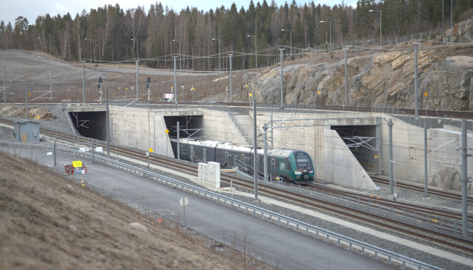 Bildet er av et tog som kjører ut fra Blixtunnelen i retning Ski. Toget er grønt og grått, og kommer ut fra den midterste tunnelen. Tunnelen til venstre er også del av samme tunnelsystem. Den til høyre er en del av den gamle Østfoldbanen.