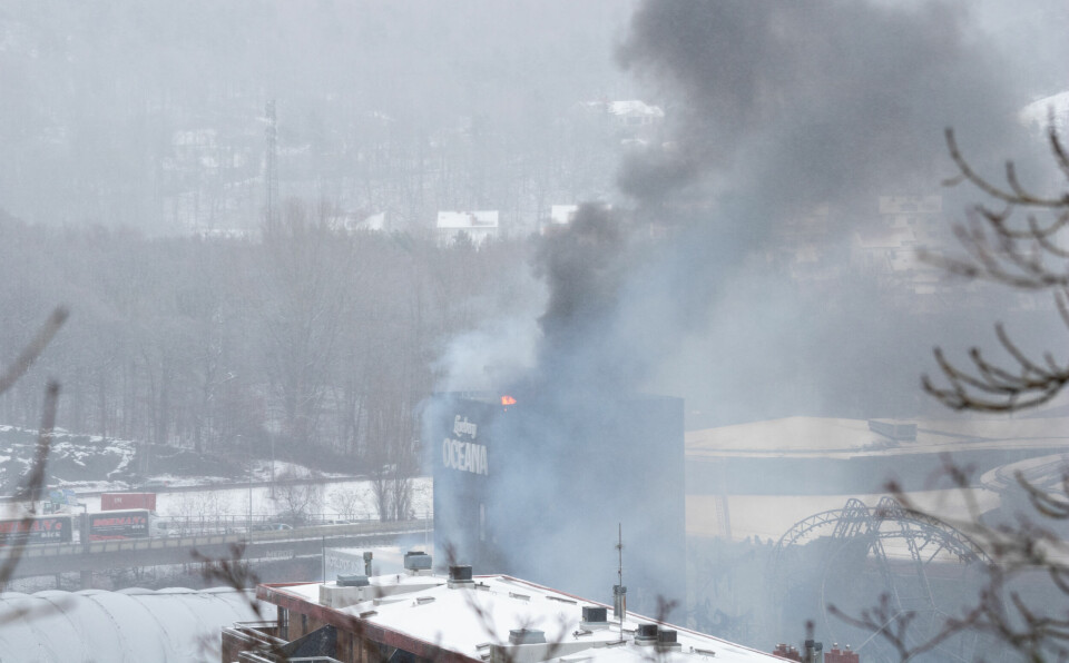 Bildet er av brannen i badelandet Liseberg Oceana. Tung, mørk røyk kommer opp fra bygget, og flammer står opp fra taket.