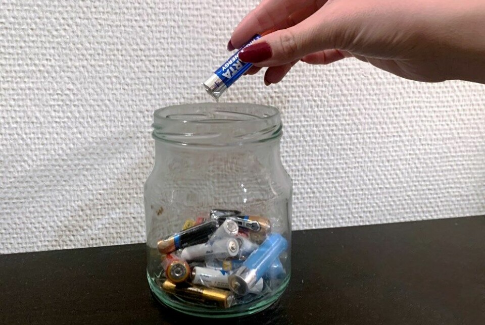 Bildet er av en hånd som putter et batteri i en glassbeholder med flere andre batterier. Polene på batteriene er tapet.